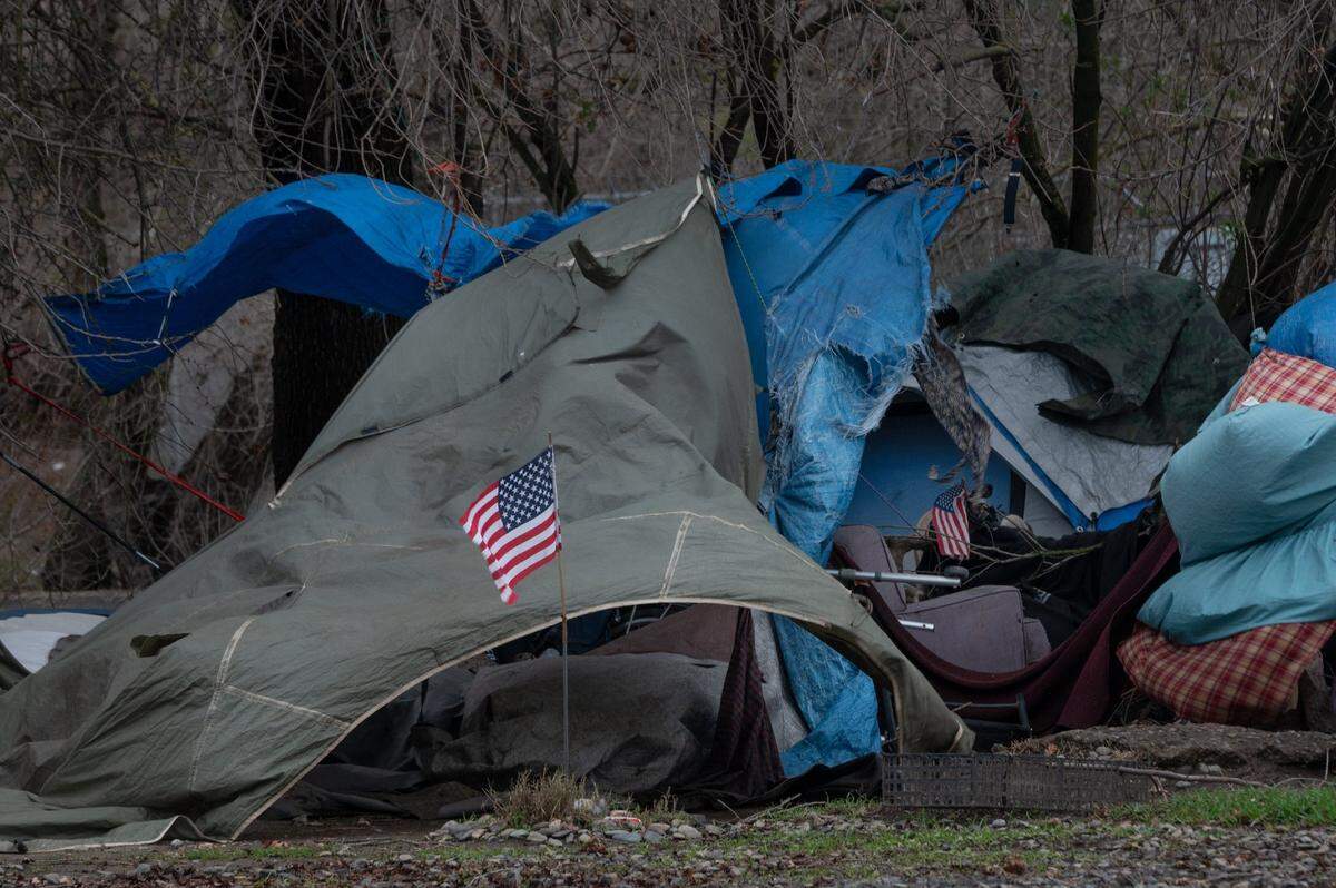 American flags blow in the wind with damaged tarps and tents at a homeless encampment near Basler and N. 18th streets in Sacramento on Wednesday, Jan. 27, 2021.