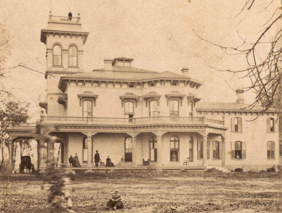 A 19th century photograph of the Bidwell Mansion in Chico shows people enjoying its front porch and a visit from a horse-drawn carriage. The landmark’s construction was completed in 1868.