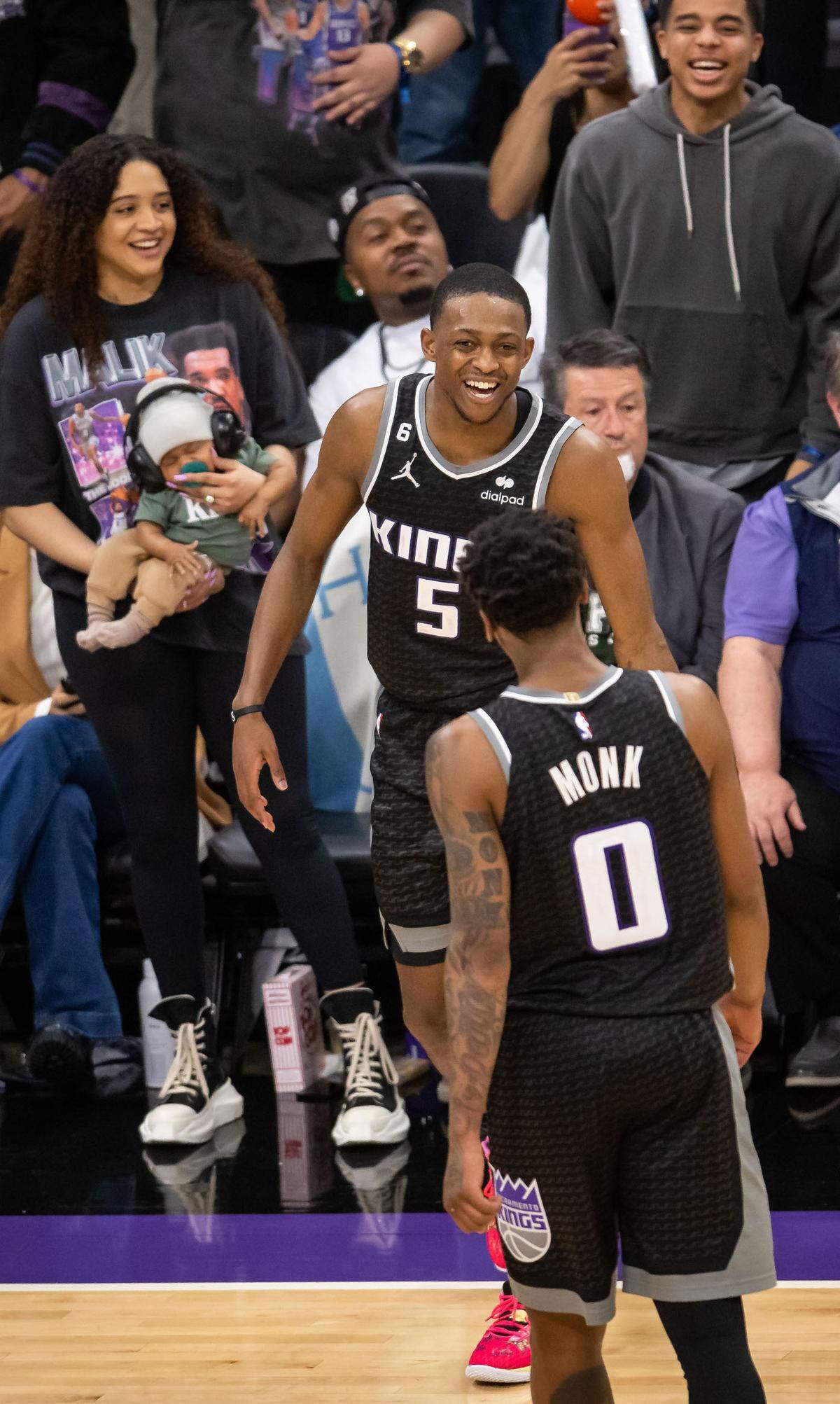 Sacramento Kings guard De’Aaron Fox (5) celebrates, with his wife and child over his shoulder, with teammate Malik Monk (0) after sinking a three point basket against the Golden State Warriors during the second half of Game 1 of the first-round NBA basketball playoff series at Golden 1 Center on Saturday, April 15, 2023.