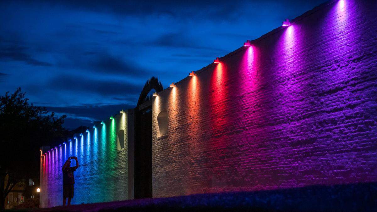 A passerby makes a photo of the special lighting recognizing Sacramento Pride Weekend illuminating the walls of Sutter’s Fort State Historic Park on Friday, June 9, 2023, presented by the Midtown Association in partnership with California State Parks and Sutter Health. The lights will be on display from dusk to dawn through June 11, and a display of red, green and gold will light the walls the weekend leading to Juneteenth.