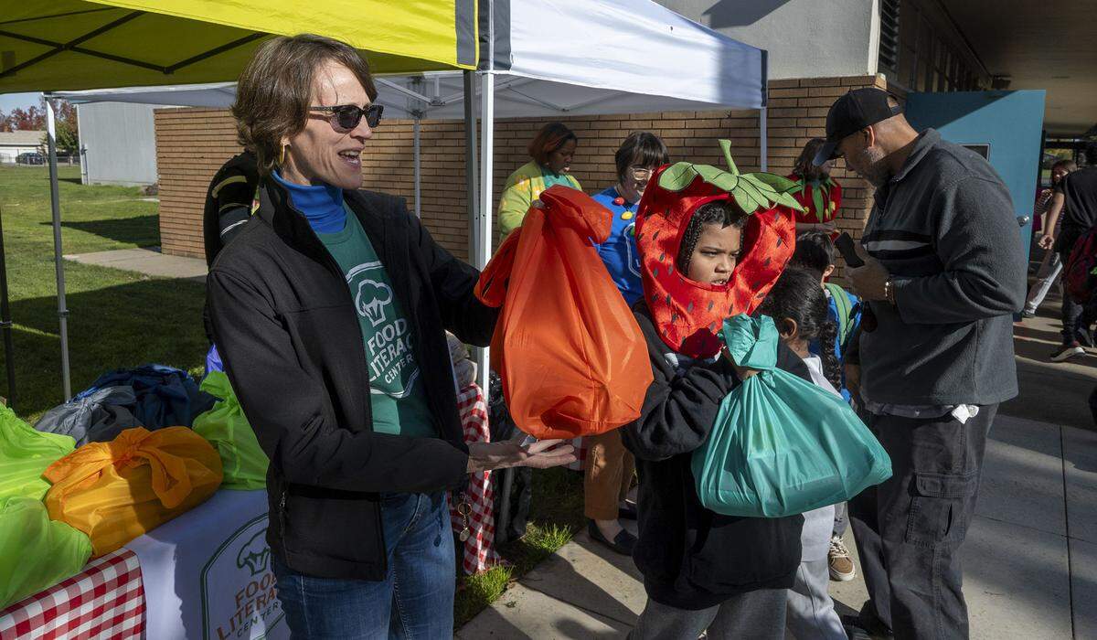 Amber Stott, left, founder of the Food Literacy Center, stands with volunteer Donovan Hall-Ramsey, 9, to hand out 50 food kits and recipes at John Sloat Elementary School earlier this month for kids to take home and cook. The Food Literacy Center Kitchen is asking Book of Dreams for $4,500 for supplies to help the program.