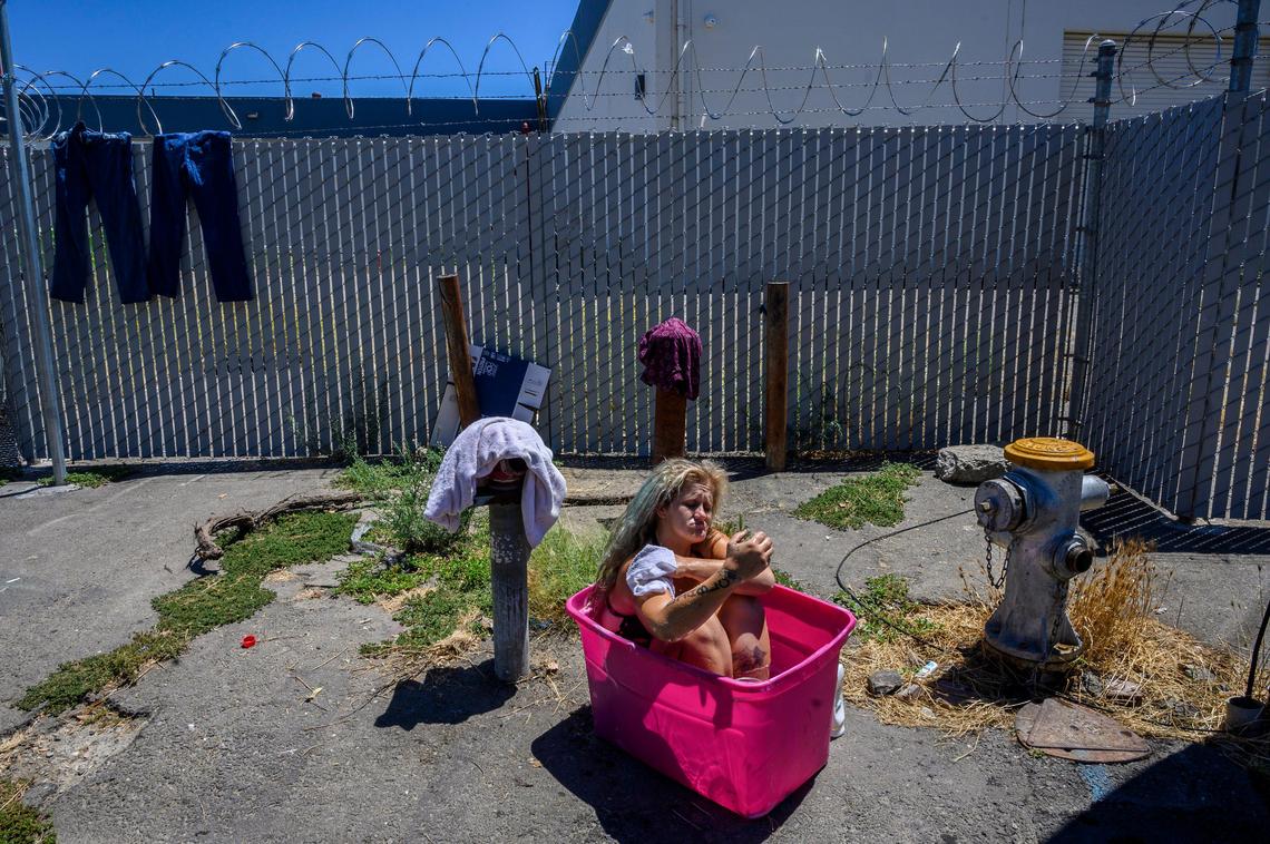Laurane Ivey, 37, sinks deep into a pink plastic tub filled with water from a fire hydrant as she begins to scrub the dirt from her worn feet. Above her is a barbed wire fence surrounding the shelter she used to live in before it closed. With no place to go she lives in her car joining other homeless in parked cars across the street including her mom Gwen Mayes, 59, who sleeps with two tiny dogs for protection. She says she wished their was a designated parking spot for the homeless with showers and portable toilets. She says she has to go to the bathroom in a bag inside her car.