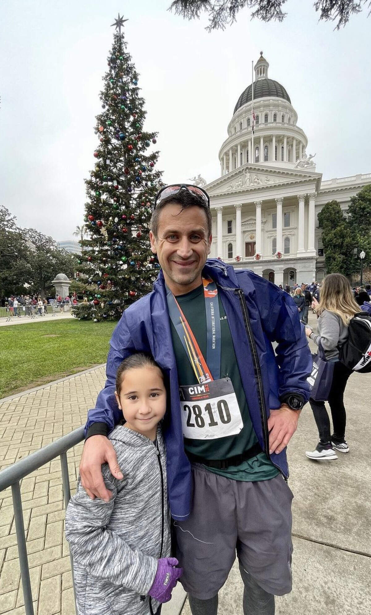 Aaron Kuen, 36 at the time, poses with his oldest daughter, Norah, in front of the Capitol in Sacramento, California, after completing the 2021 California International Marathon on Dec. 5, 2021. Kuen finished the 26.2-mile race with a time of 3:05:53.