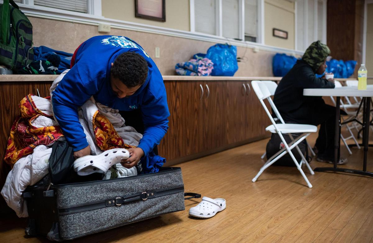 Giovanni Bowden repacks a suitcase after taking out indoor shoes while his partner Mahogany Lenard eats a hot meal behind him at Elk Grove United Methodist Church, a recently opened Elk Grove Overnight Warming Center, on Friday, Dec. 10, 2021, at 8986 Elk Grove Blvd. The shelter is open through Tuesday at the church for people experiencing homelessness or inadequate heat in their home.