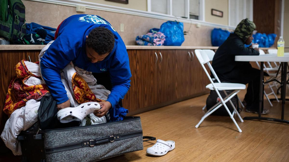 Giovanni Bowden repacks a suitcase after taking out indoor shoes while his partner Mahogany Lenard eats a hot meal behind him at Elk Grove United Methodist Church, an Elk Grove Overnight Warming Center, on Friday, Dec. 10, 2021, at 8986 Elk Grove Blvd. The shelter is open through Tuesday at the church for people experiencing homelessness or inadequate heat in their home.