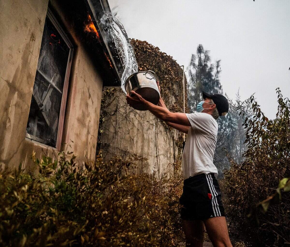 Brooks Corrigan of New York throws a pot of water to extinguish a flame burning his father’s neighbor’s property in Calistoga on Monday.