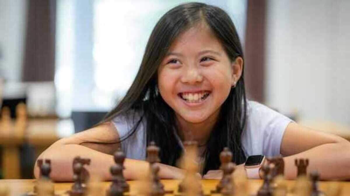 Rochelle Wu smiling in front of a chess board. Wu earned the title of International Chess Federation Master in 2022.
