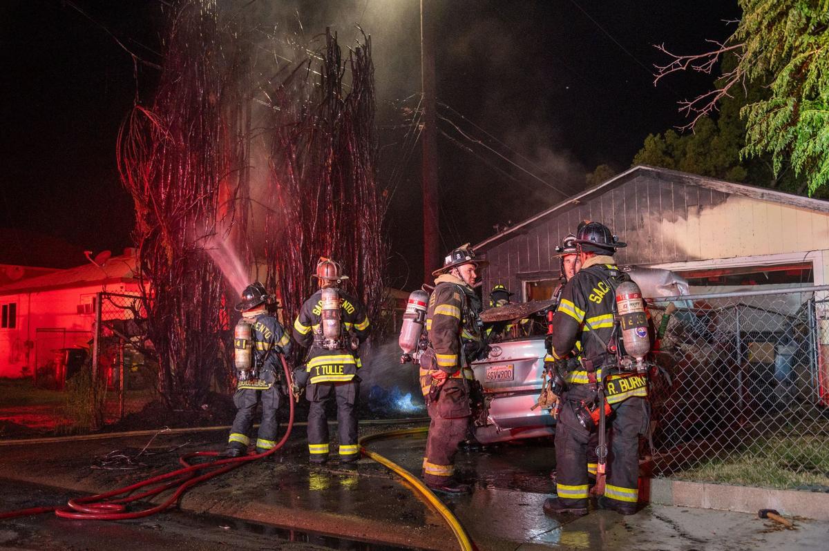 Sacramento firefighters hose down a burnt tree on the 4500 block of Perry Avenue in Sacramento on Thursday night. Flames started in a vehicle fire before spreading to a nearby structure and some surrounding foliage, though the cause remains unknown according to the Sacramento Fire Department.
