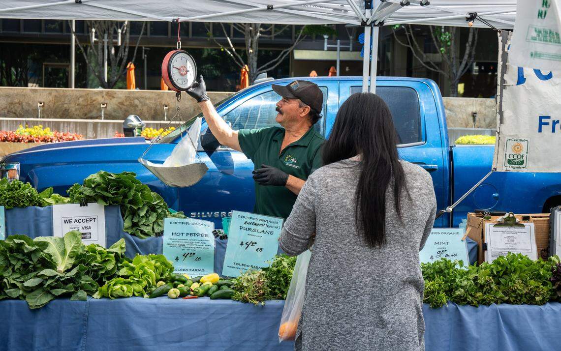 Federico Toledo weighs a bag of produce for a customer at his stand, Toledo Farms, at the Capitol Mall Farmers’ Market on Wednesday.