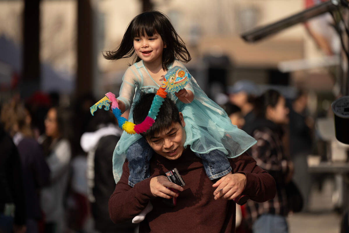 Mia Her, 3, rides on the shoulders of her father Hou Her as she holds a paper dragon she put together at the Elk Grove Lunar New Year in Old Town Plaza on Saturday.