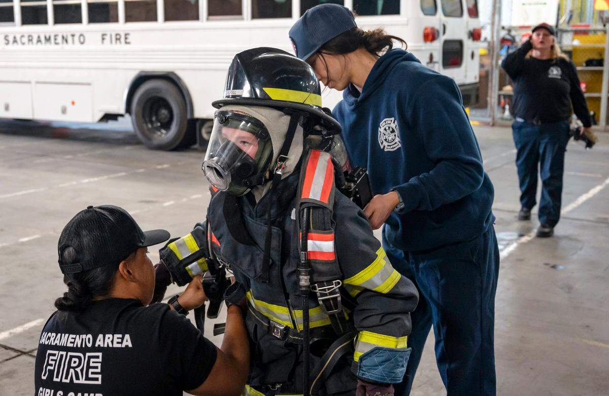 Reese Blankenship, 10, is helped by Lyneeka Boyd, left, a reserve with the Sacramento Fire Department, and Casilia Loessberg, of the San Jose Fire Department, put on the air tank at the Sacramento Area Girls Fire Camp at McClellan Park on Saturday, Oct. 23, 2021. It changed my life, Loessberg said about attending the first Sacramento camp in 2018.