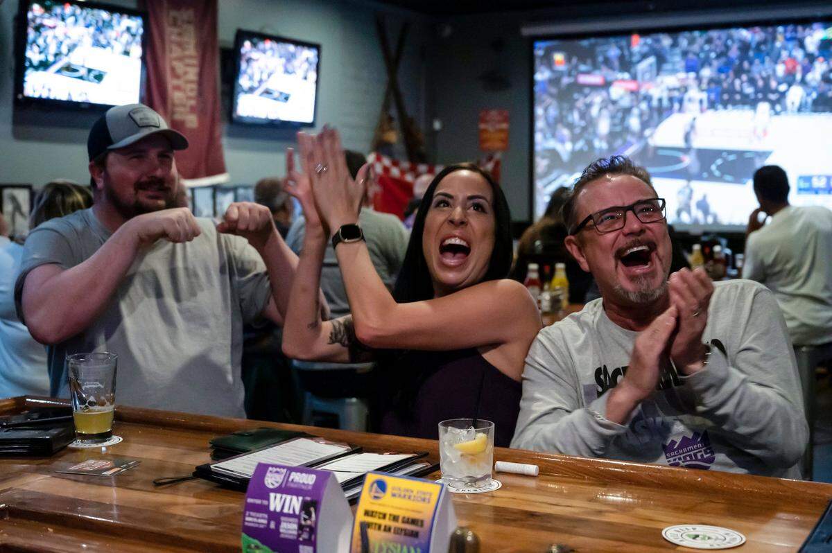 Scott Parsons, left, tries to fist bump Meredith Mitchell as she cheers with her husband Tim Lee, right, after Sacramento Kings guard Davion Mitchell makes both free throws in the first half of game two against the Golden State Warriors on Monday, April 17, 2023, at Field House American Sports Pub in Arden Arcade.