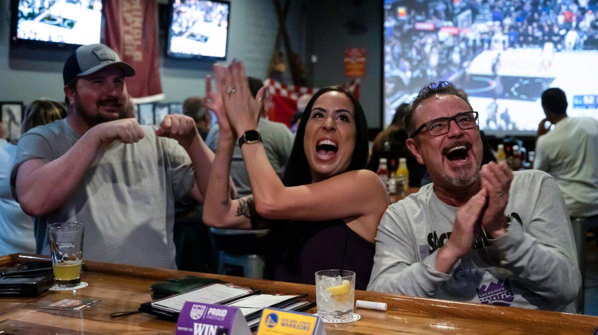 Scott Parsons, left, tries to fist bump Meredith Mitchell as she cheers with her husband Tim Lee, right, after Sacramento Kings guard Davion Mitchell makes both free throws in the first half of game two against the Golden State Warriors on Monday, April 17, 2023, at Field House American Sports Pub in Arden Arcade.