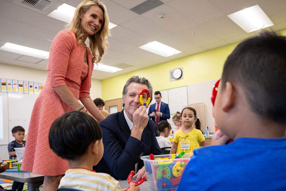 Gov. Gavin Newsom, joined by First Partner Jennifer Siebel Newsom, and a transitional kindergarten student peek at each other through plastic educational toys in August at Miwok Village Elementary School in Elk Grove, during an event to highlight the state’s plans to increase culturally competent instruction, nutrition initiatives, health care, counseling and before- and after-school programs.