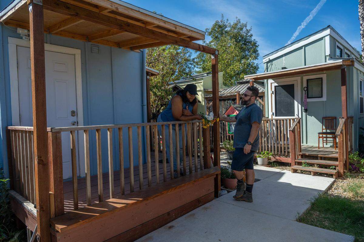 Robin Moore, left, who founded a tiny home community in her backyard, visits with Maximilian Rosa, right, director of the Sierra Service Project, who helped create a community garden adjacent to her home on Friday, Oct.11, 2024 in Del Paso Heights. The garden supplies vegetables, fruit and flowers for the shelter residents.
