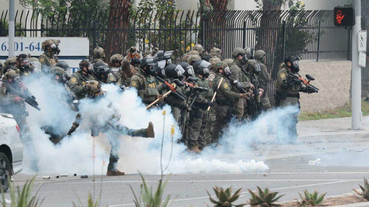 Federal law enforcement officers kick tear gas back to the crowd as people block off the street and set a fire during protests against ICE and immigration raids on Saturday, June 7, 2025, in Paramount.