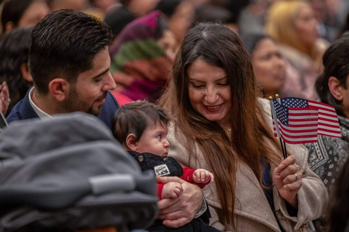 Baby Lucas, dressed in red, white and blue, is fascinated by his mother Sandra Toma’s two American flags while sitting on father Rimon Toma’s lap during the naturalization ceremony Wednesday. The family is originally from Iraq.