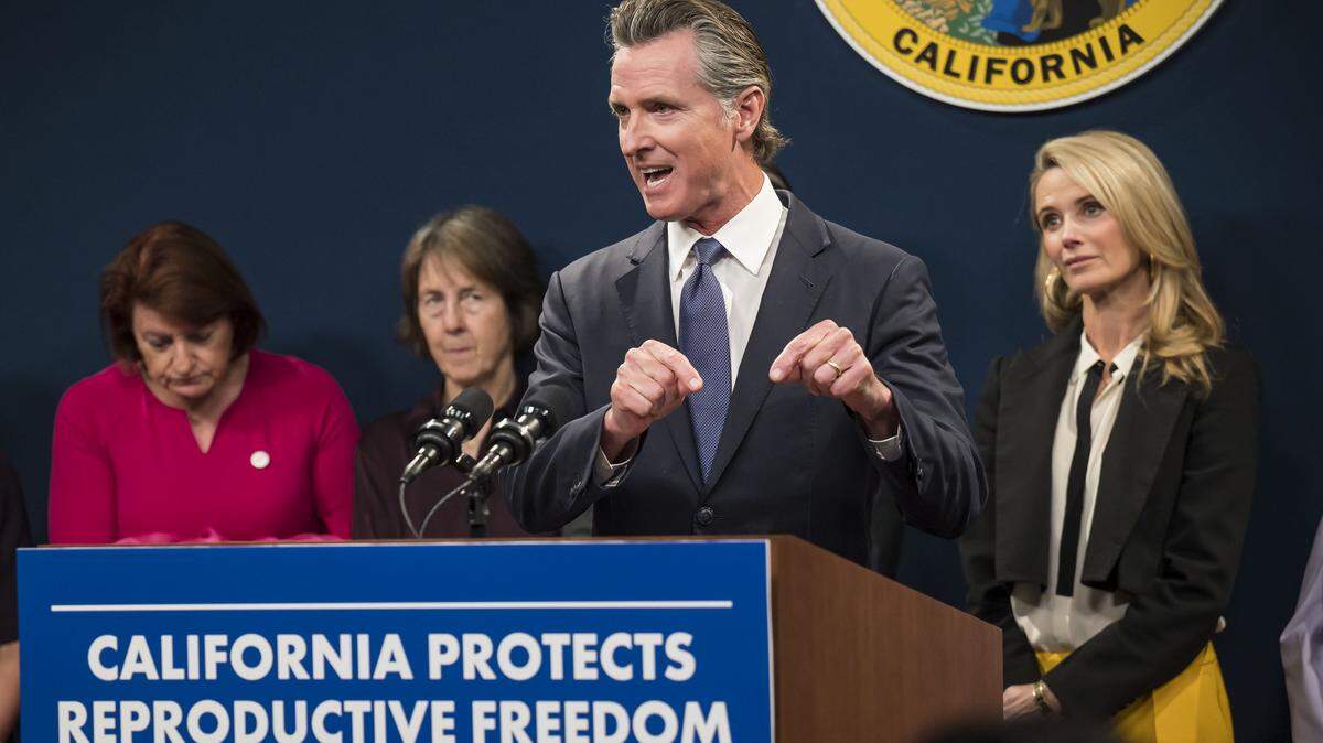 Gov. Gavin Newsom speaks Tuesday, April 18, 2023, at the Capitol swing space in Sacramento on actions the state is taking to protect women’s reproductive rights. Over his shoulder, from left,  Senate President Pro Tem Toni Atkins, D-San Diego, Sen. Nancy Skinner, D-Berkeley, and First Partner Jennifer Siebel Newsom stand after giving their own remarks — along with reproductive rights stakeholders — at the news conference held the day before an anticipated U.S. Supreme Court ruling on abortion medication.