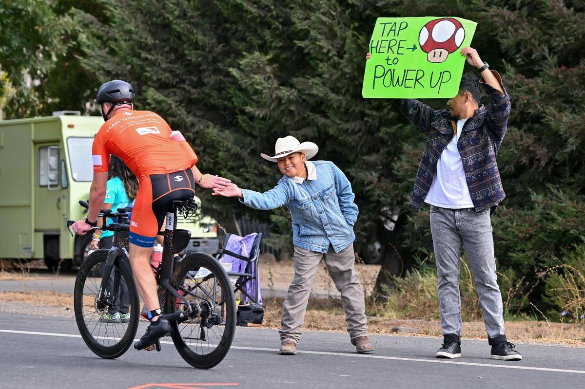 Alvin Saguin of Los Angeles holds a sign for participants while his cousin Marcelo Gino, 10, high-fives Josh Folkerts of Chicago near the 38-mile marker of the bike course in Yolo County.