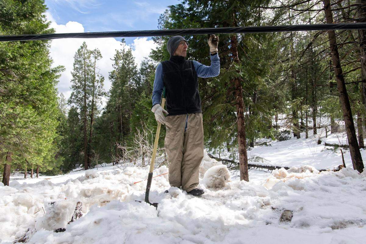 Bob Cammer touches a damaged phone line on Alpine Drive in Magra on Tuesday. Cammer has been without power for almost a week. He said he pitched a tent inside his house to stay warm, with temperatures dropping to 38 degrees.