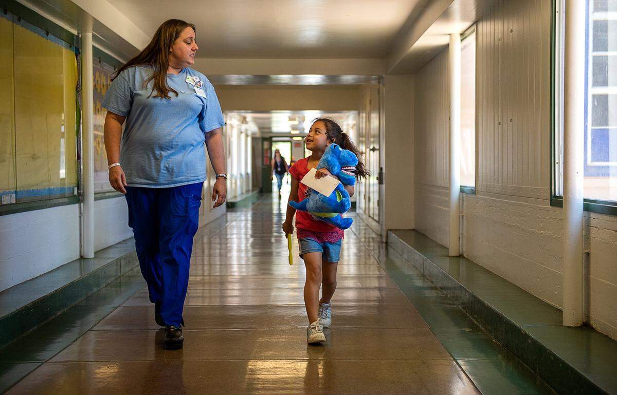 First grader Stephanie Rojas, 7, walks back to her class with dental coordinator Gizelle Jacobs after a dental visit at the Northwood Elementary School in Sacramento in May 2019. The participates in Every Smile Counts, a test program that places hygienists in schools – currently closed because of coronavirus concerns – and pediatricians’ offices to make it easier for Medi-Cal patients to receive dental education and services.