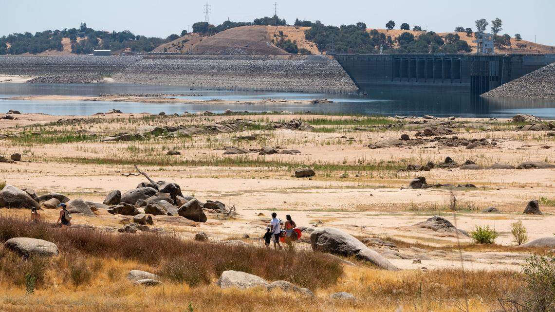 People cross the dry bottom of Folsom Lake to reach its shore near Beal’s Point on a scorching Saturday, July 10, 2021, the same day downtown Sacramento reached 113 degrees for a daily record, according to the National Weather Service.