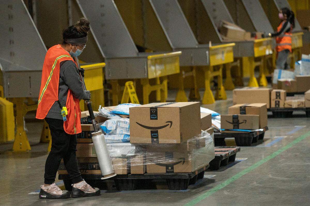 A worker at the Amazon fulfillment center in Tracy wraps a pallet with packages Friday that were sorted by a new team of robots that move autonomously loaded packages with robotic arms.