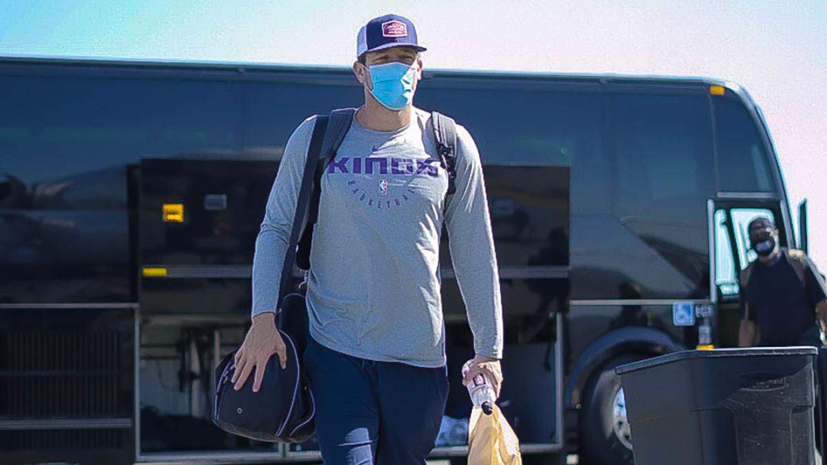Kings coach Luke Walton walks from a chartered bus to an airplane Wednesday for the trip to Florida for the NBA’s restart of the regular season.