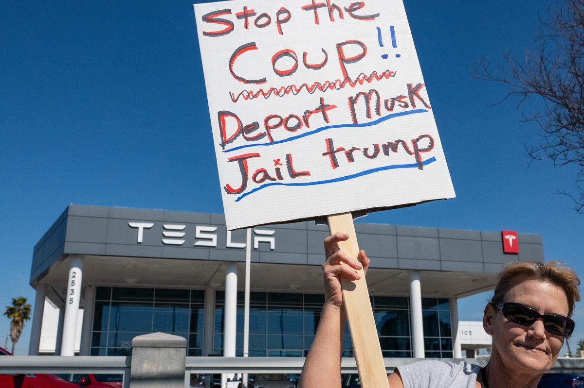A demonstrator holds a sign calling for the deportation of Elon Musk at a Tesla dealership on Arden Way near Sacramento on Saturday, March 8, 2025. More than 100 people lined both sides of street to protest the role of the tech billionaire and Tesla CEO in the Trump administration.