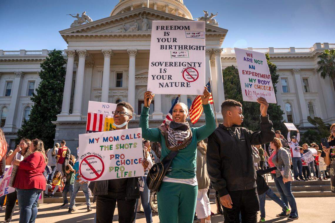 “My mom calls the shots” reads a sign held by Jordan Strong, left, as he protests COVID-19 vaccination mandates for children with his mother Lakita and brother Jayden at the state Capitol on Oct. 18.