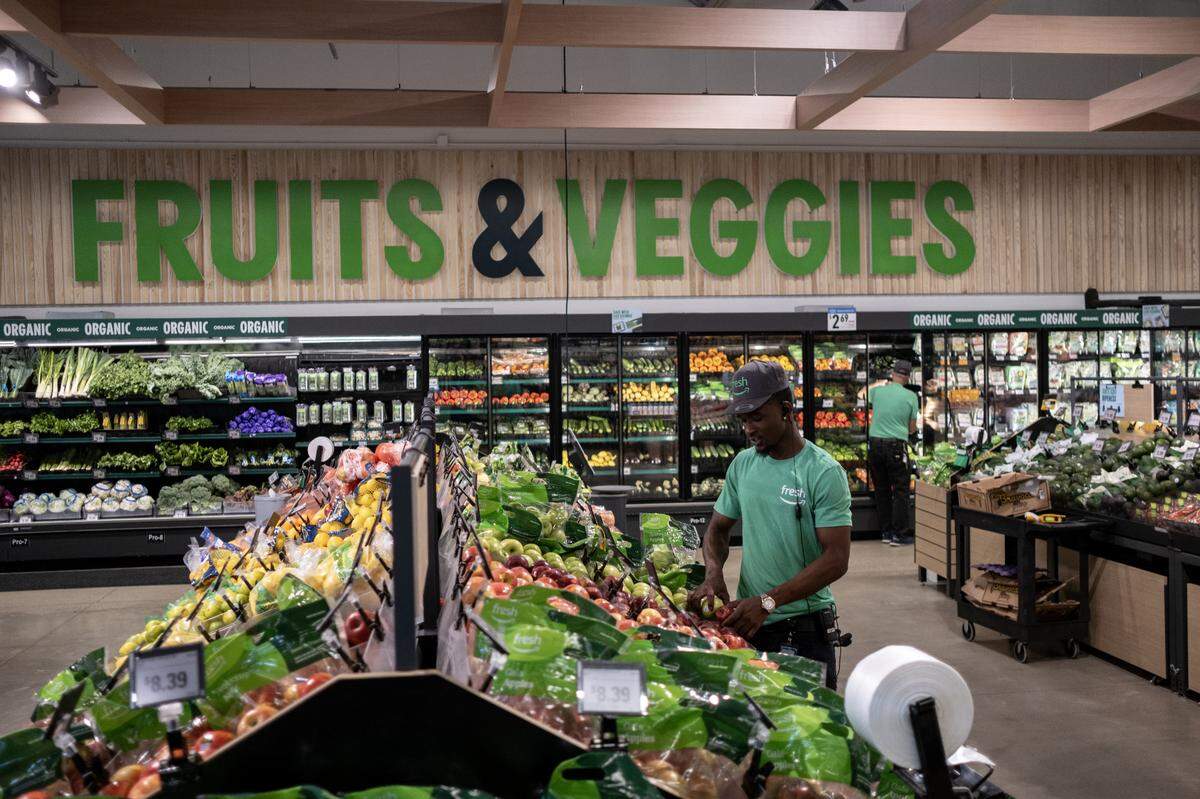 An Amazon Fresh employee stocks produce inside the grocery store.