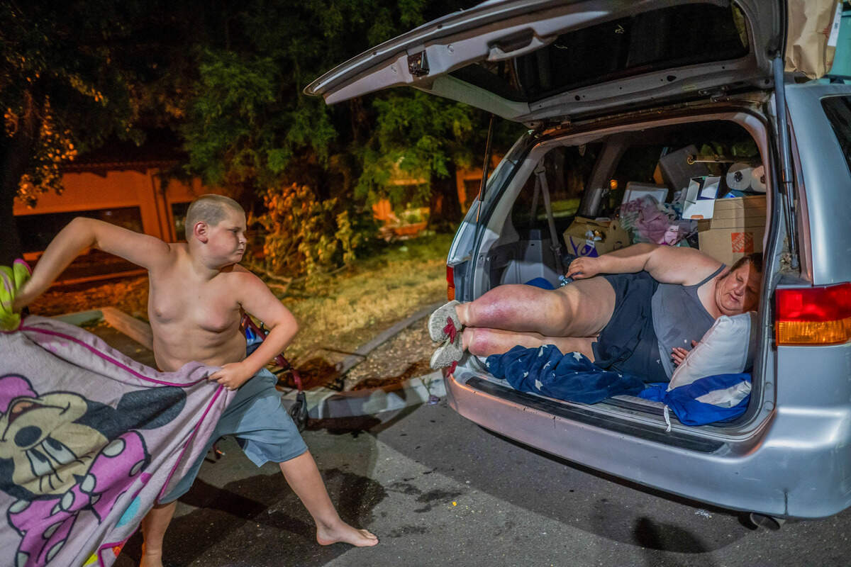 Shortly after midnight, Keith-Dalton Smith, 11, tosses a blanket featuring the Disney character Mickey Mouse to his mother, Amy Heckart, 46, who is disabled, as they prepare to sleep in the back of their van on Thursday in Sacramento. The family had lived at the Motel 6 for the past 2-1/2 years through a city-funded shelter program.