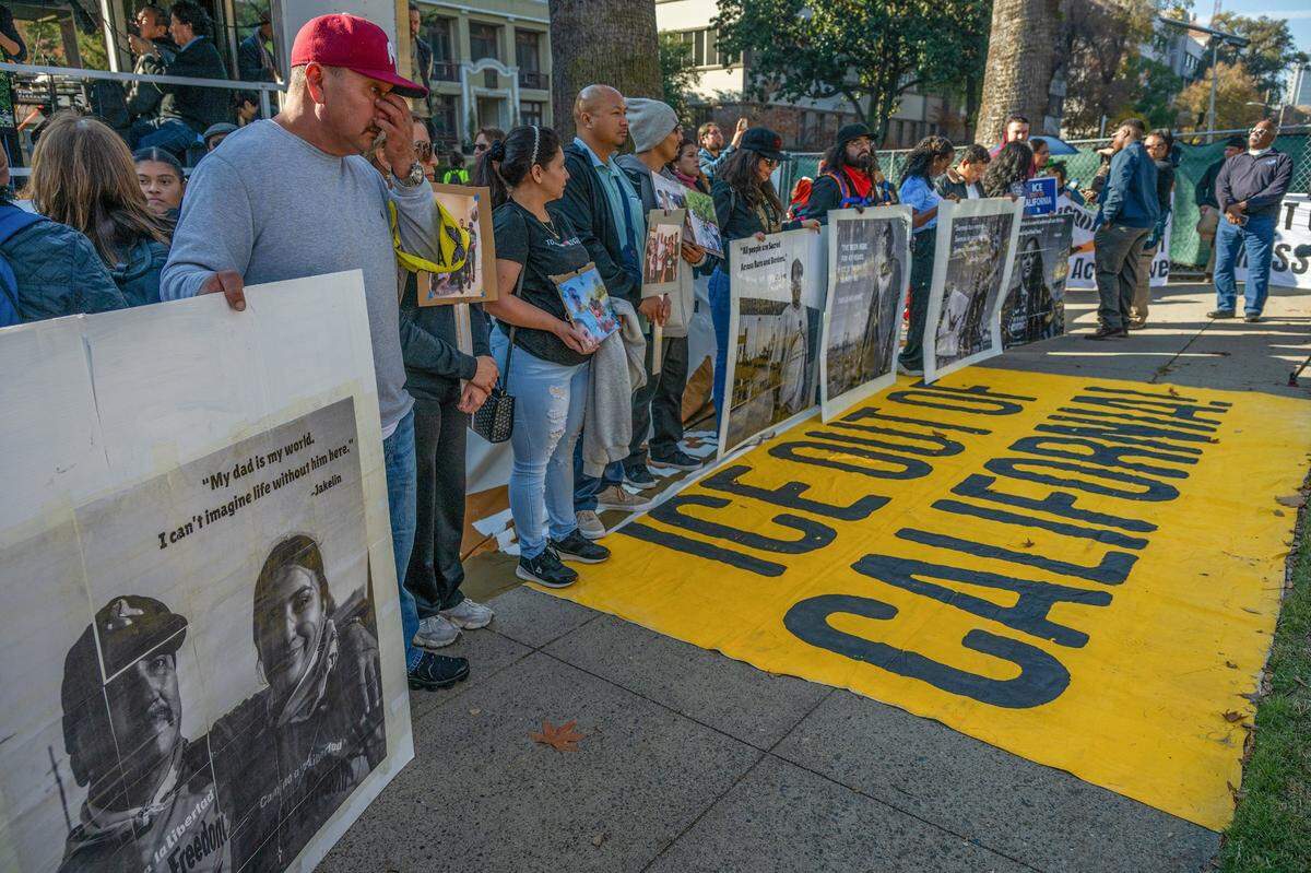 Jesus Prieto, left, of Sacramento, wipes tears as he holds a poster with his photograph as he joins hundreds at a rally to oppose mass deportations and protect immigrant Californians at the state Capitol in December. On the ground, a yellow flag calls for the removal of the federal Immigration and Custom Enforcement agency, or ICE, from the state.