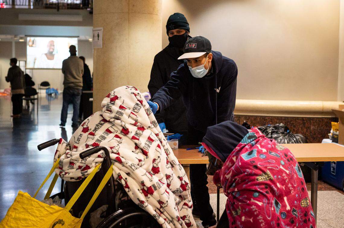 Daniel Castillo, volunteering with Hands on Sacramento, does a temperature check — part of the standard precautions taken amid the coronavirus pandemic — on homeless people coming into the warming center at Tsakopoulos Library Galleria as they escape the inclement outside Wednesday, Jan. 27, in downtown Sacramento.