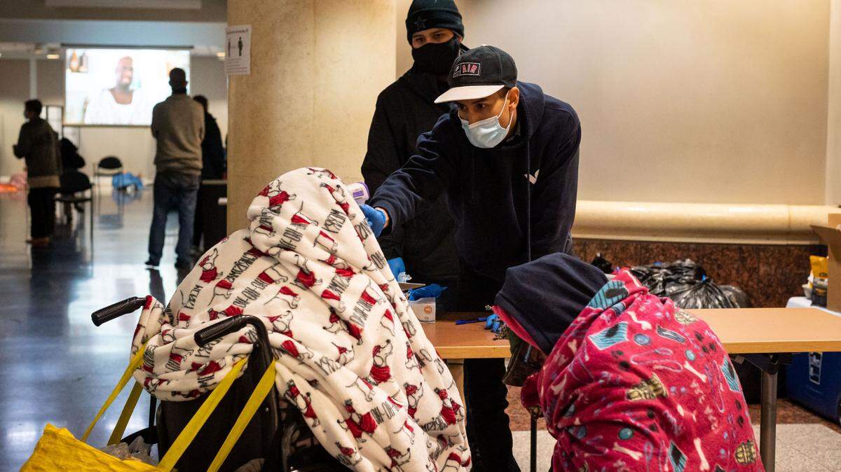 Daniel Castillo, volunteering with Hands on Sacramento, does a temperature check — part of the standard precautions taken amid the coronavirus pandemic — on homeless people coming into the warming center at Tsakopoulos Library Galleria as they escape the inclement outside Wednesday, Jan. 27, 2021, in downtown Sacramento.