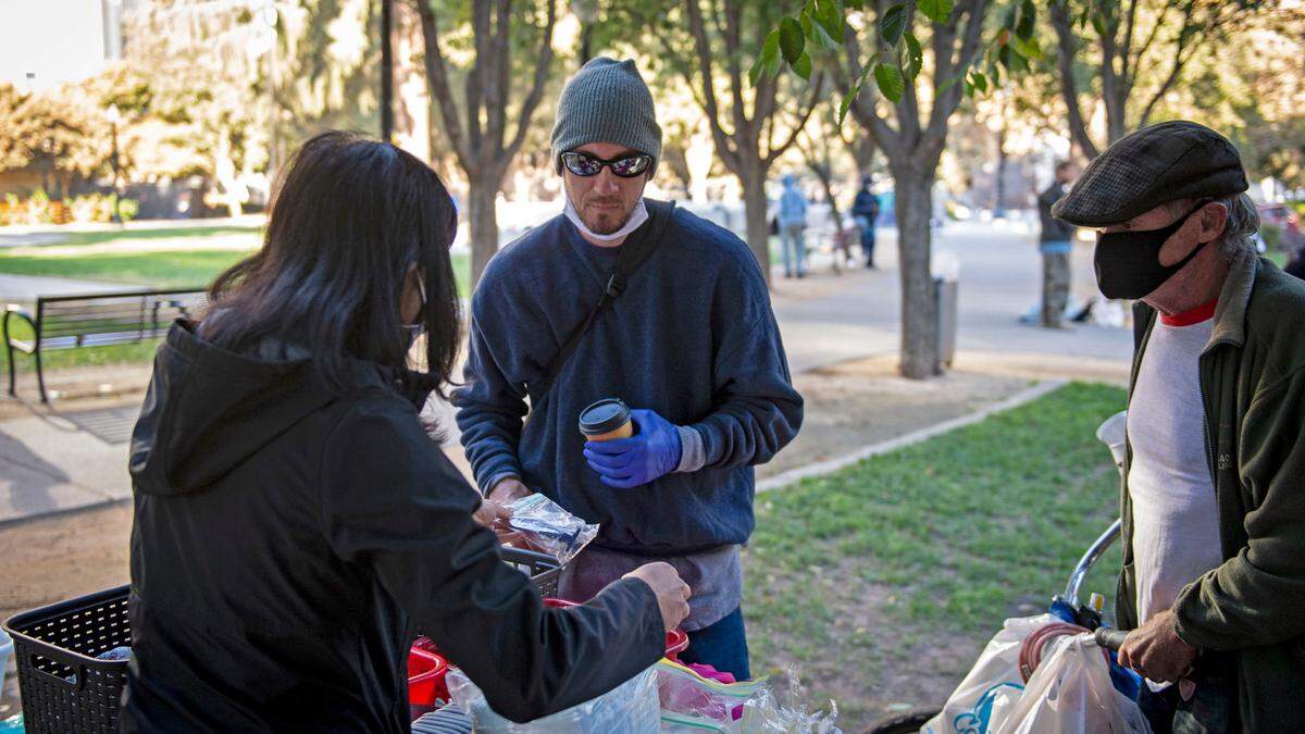Adam Green, center, receives some toiletries after standing in line Saturday morning, Oct. 31, in Cesar Chavez Plaza with a few dozen other homeless individuals at a makeshift soup kitchen set up by a church group,.