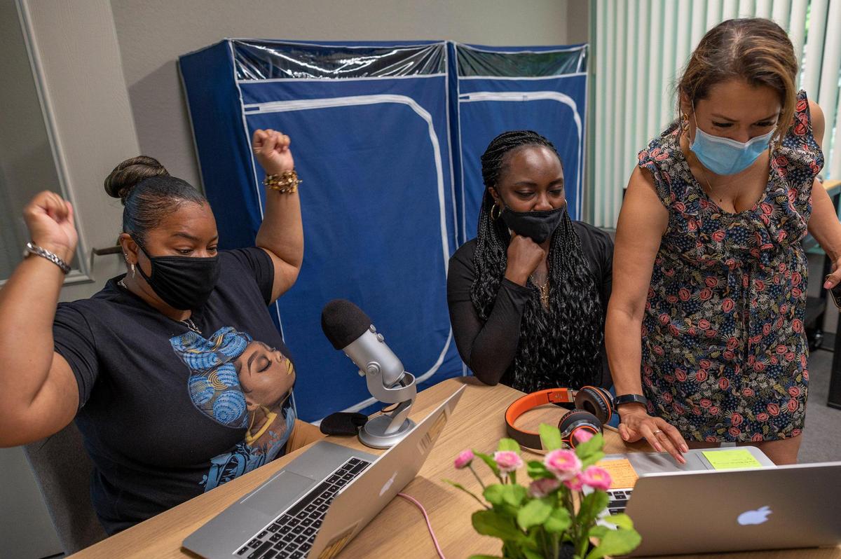 As Norma Cumpian, right, troubleshoots a computer problem during the taping of a Free World podcast co-host Shone Robinson, left, celebrates her success before their interview with Candace Lewis, center, at the Anti-Recidivism Coalition office on Friday, July 30, 2021, in Sacramento. The podcast is about women reconstructing their lives after incarceration. All three women were once incarcerated.