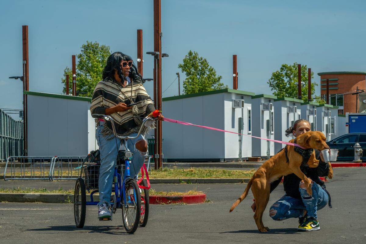 Tracy Williams, 51, holds onto her leashed dog, Sassy, as case manager Samantha Vegin gives the dog a drink at Sacramento County's Stockton Boulevard Safe Stay Community in April. Williams, who has been homeless off and on for at least 25 years, said she feels safe in the community. “As a woman, it’s nice to be able to lock your doors,” she said.
