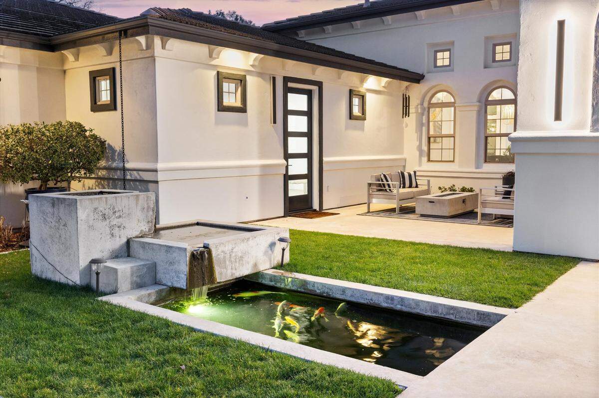 In the front of the Sacramento area house, a gated courtyard welcomes visitors with a modern streamlined water feature and “low-maintenance” koi pond.