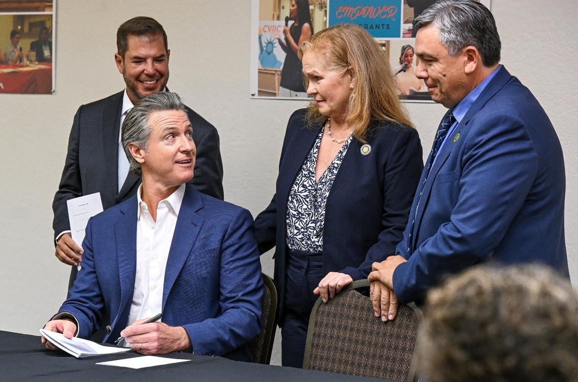 Gov. Gavin Newsom, seated, looks back toward assemblymembers Joaquin Arambula, from left, Gail Pellerin and Juan Carrillo while signing Assembly Bill 2240, a farmworker housing bill, ensuring that farmworkers and their families are not forced to leave housing centers because of outdated requirements, during a signing ceremony in Fresno on Tuesday.