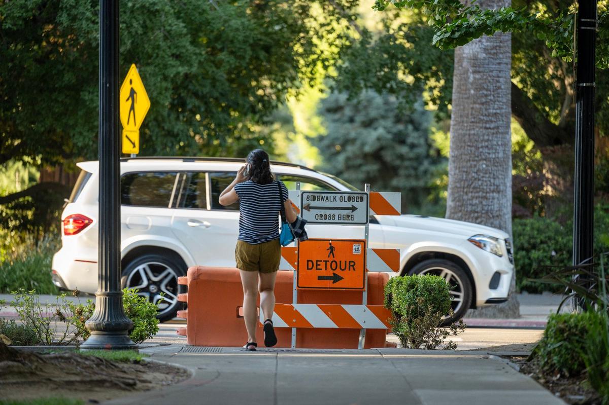 A pedestrian waits to cross through the sidewalk closure at 14th and N streets closed by the City during the Capitol construction in downtown Sacramento on June 28.
