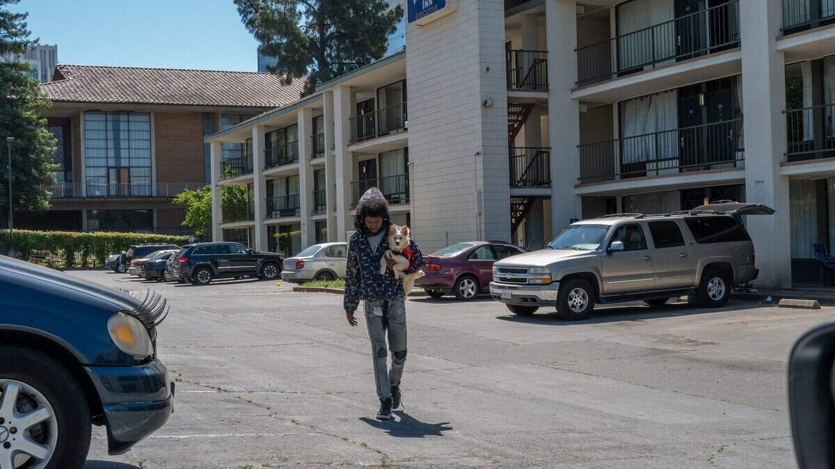 Project Roomkey participant Benjamin Frazier, 26, holds his dog Ralphie as he walks across the parking lot of the Vagabond Inn motel in Sacramento on Wednesday, May 17, 2023. “This is very depressing,” he said about the program shutting down, although he said his room had black mold and cockroaches.