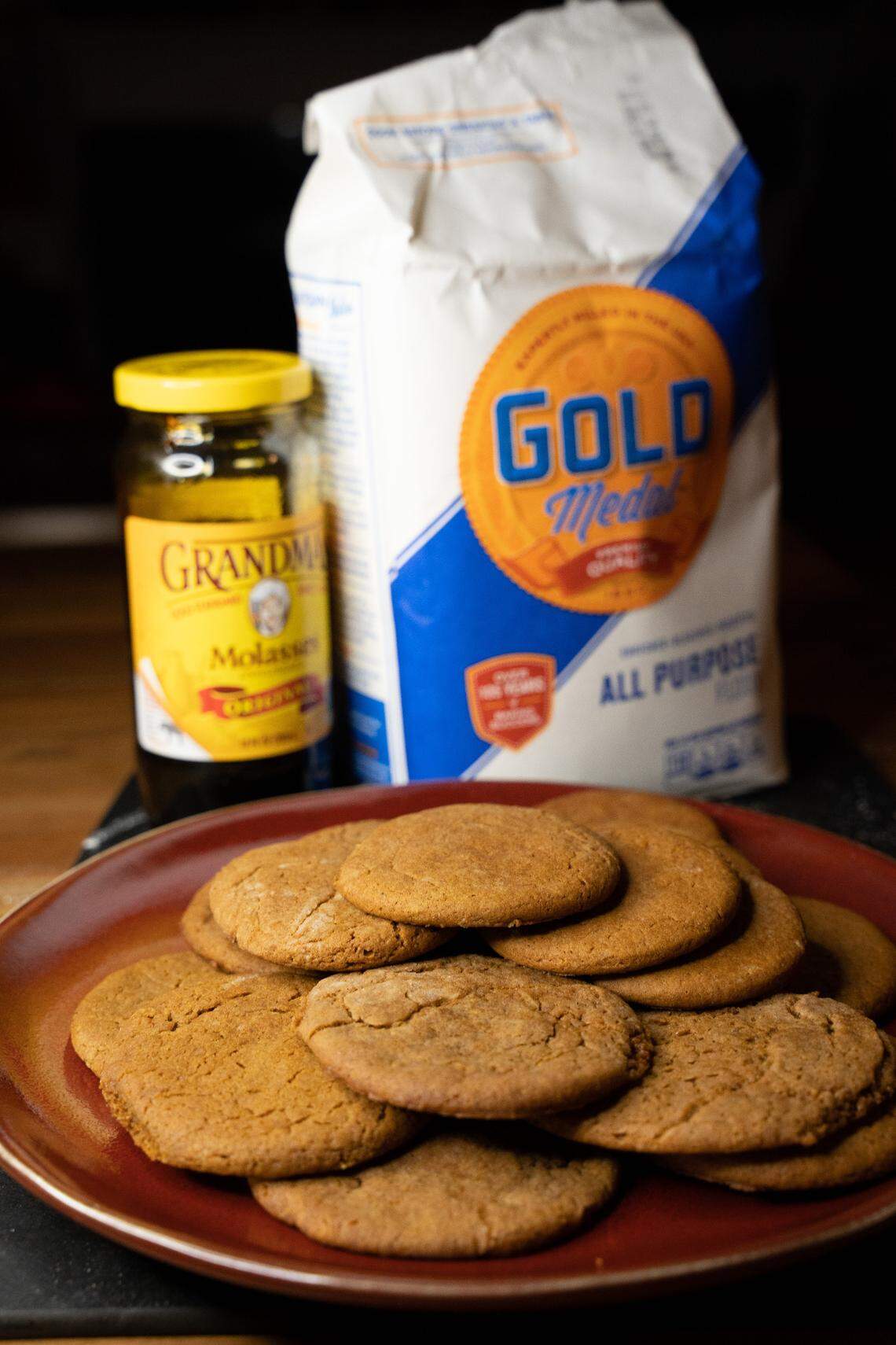 Molasses ginger cookies pictured in front of a jar of molasses and a bag of flour.