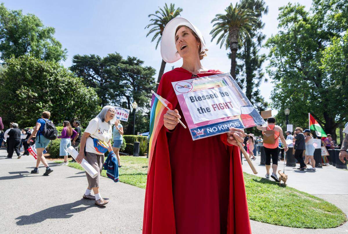 Tiffany Day of Penn Valley carries a “Blessed be the fight” sign while dressed as a character from “The Handmaid’s Tale” during the “No Kings” protest in the Capitol in Sacramento on Saturday, June 14, 2025. 