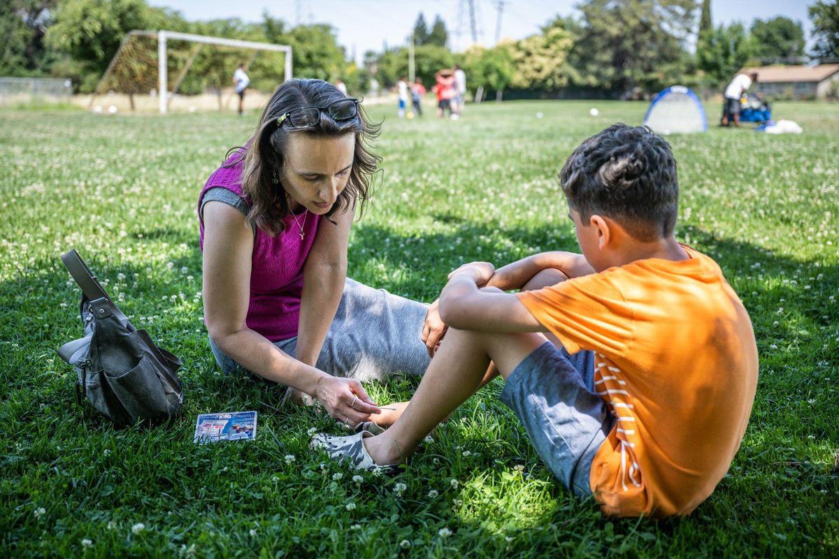 Rena Crocker, executive director of The GreenHouse, tends to an injured foot as kids in the program play soccer at Niños Park on Monday.