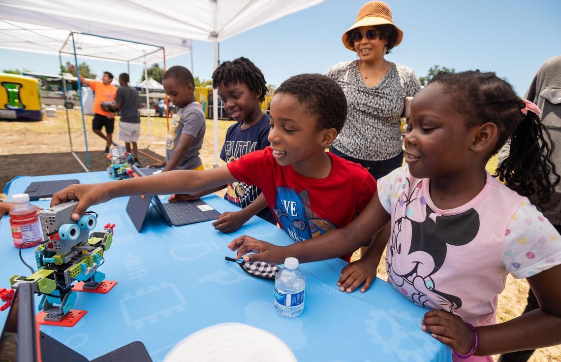 Seven-year-old twins Efe, center, and Ese Eboigbe, right, of Sacramento, interact with one of the Jimu MeeBots, an educational coding and modeling robotic kit, at a Square Root Academy table during the H@ck the Park outdoor festival Saturday, July 9, 2022, at Maple Park in Sacramento. The annual event returned for its third year after a hiatus due to the COVID-19 pandemic, and added an arts component to promote Science, Technology, Engineering, Arts and Mathematics in underrepresented communities.