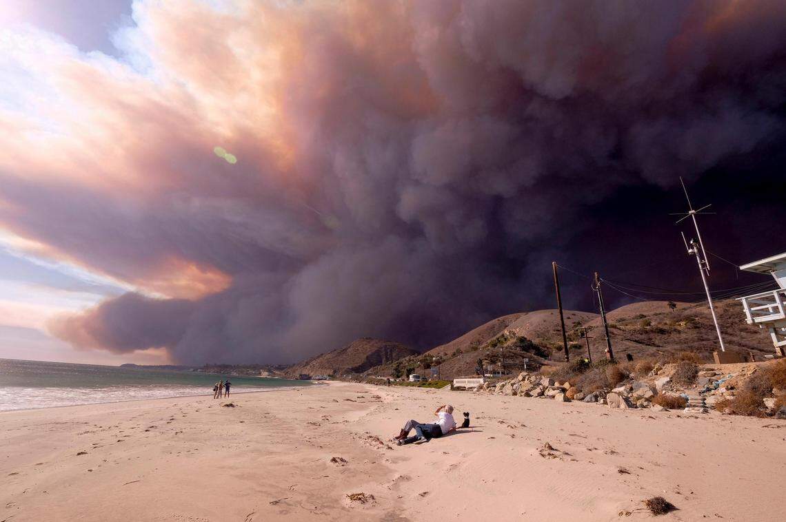People enjoy the day in the beach as the heavy smoke rises over the the Santa Monica Mountains during the Woolsy fire in Malibu, Calif., Friday, Nov. 9, 2018. (AP Photo/Ringo H.W. Chiu)