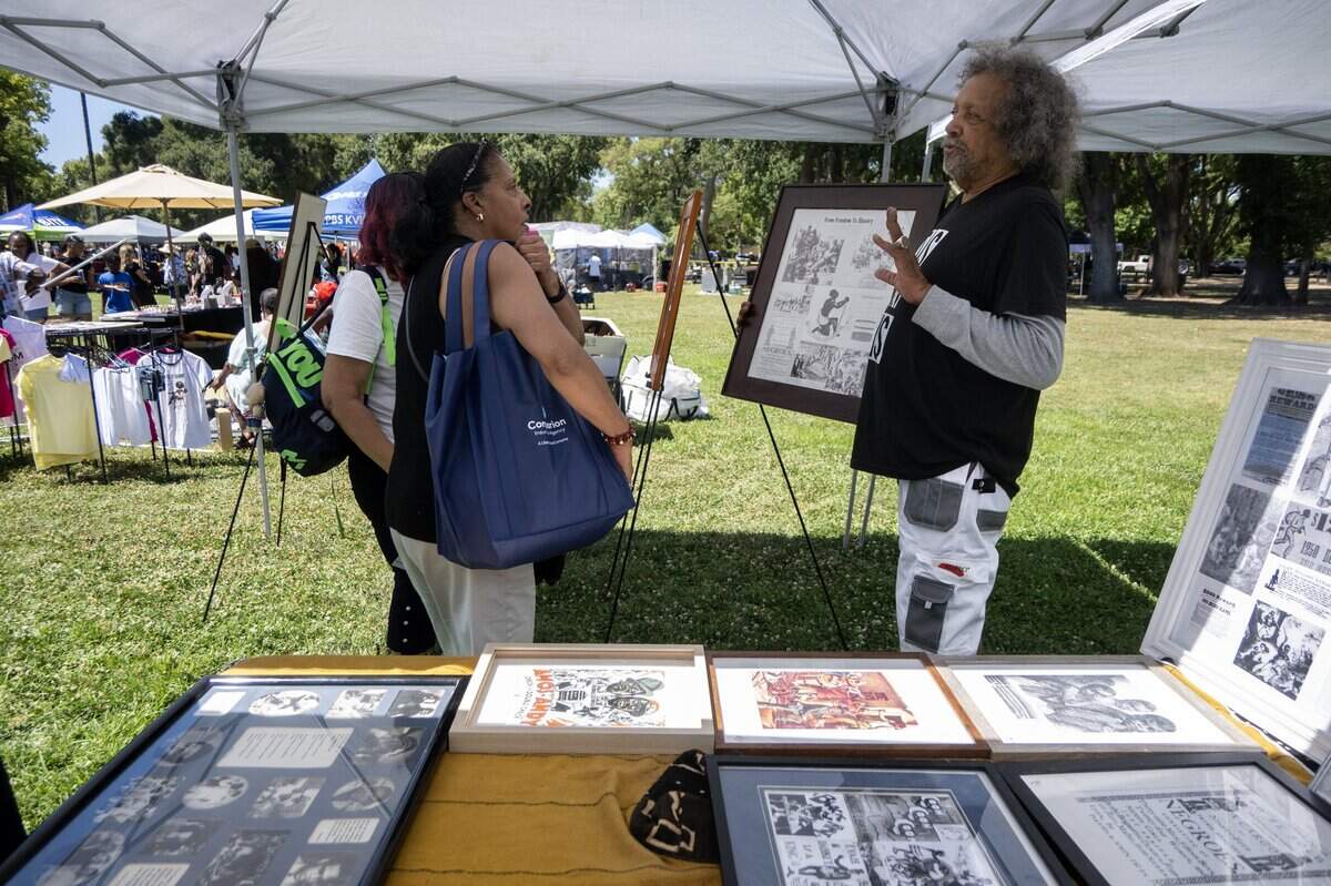 Richard Henry of Oakland explains his traveling exhibit on slavery in America, “Forgive Yes, Forget Never” to Kathaleen Graham during the Juneteenth event in Land Park on Saturday, June 20, 2026, in Sacramento.