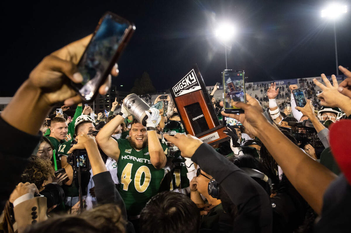Sacramento State Hornets defensive lineman Killian Rosko (40), left, raises the Causeway Classic prize alongside a conference trophy while players, students and fans rush the field after their win over UC Davis in 2022.