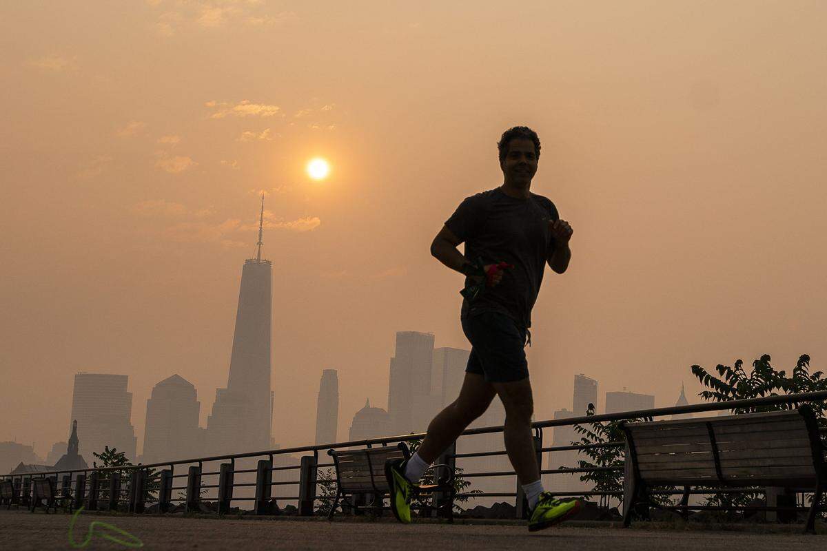 The One World Trade Center and the New York skyline is seen in the background as a man jogs through the Liberty State Park while the smoke from Canada wildfires covers the Manhattan borough on Thursday, June 8.